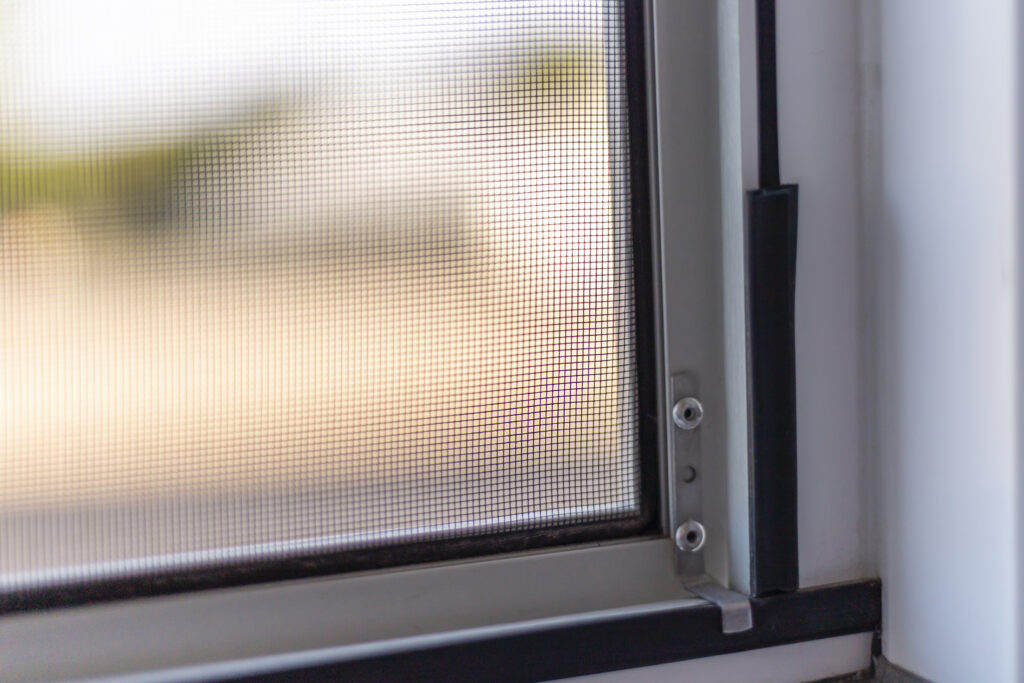 Sunlight streams through a fine mesh window screen, creating a warm and inviting indoor ambiance. The screen's details offer protection from flies while allowing light to filter in